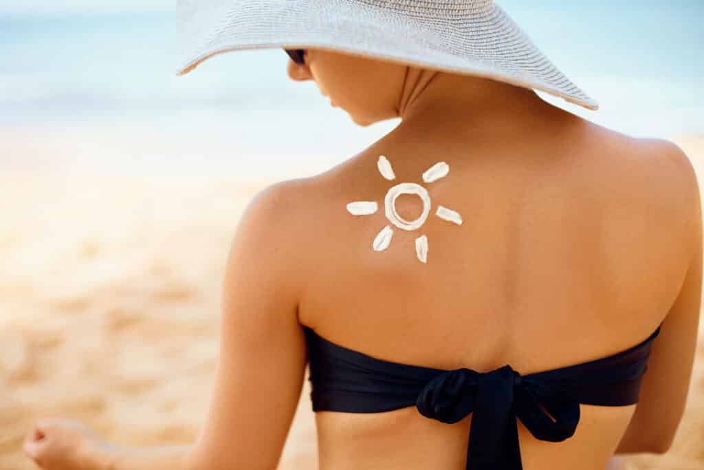 Sun cream on tanned shoulder. Sun protection. Beautiful woman in bikini applying Solar Cream. Skin and body care. Portrait of female holding suntan lotion and moisturizing sunblock.